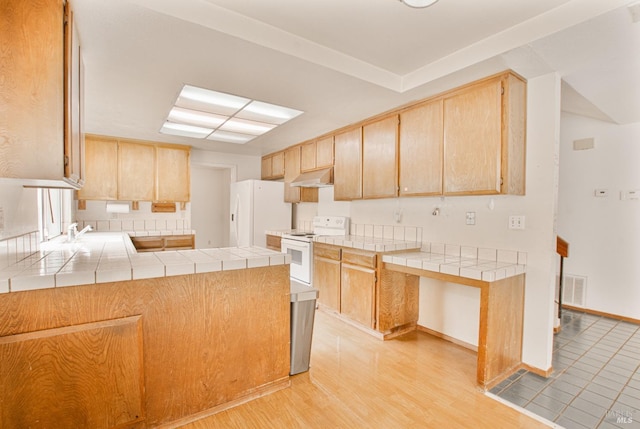 kitchen with white appliances, under cabinet range hood, tile countertops, and a sink