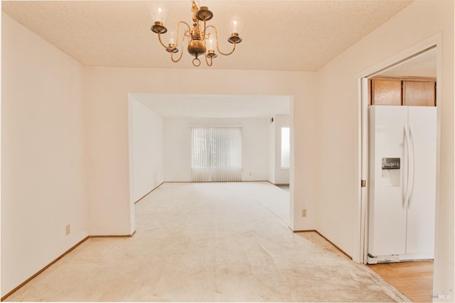 spare room with a chandelier, light carpet, and baseboards