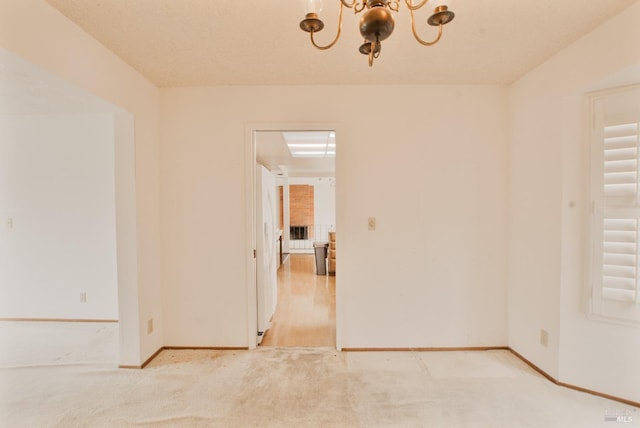 spare room featuring baseboards, a chandelier, and light carpet