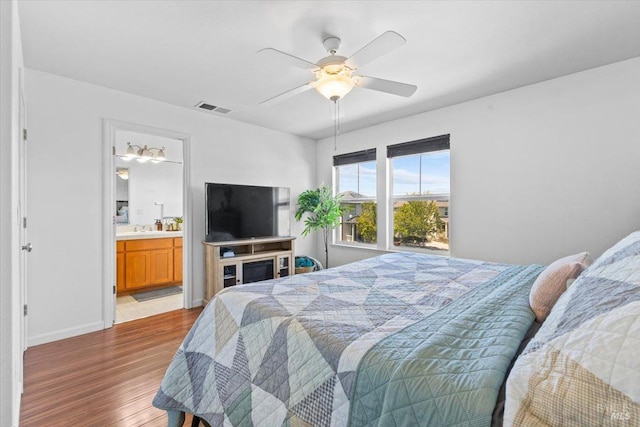 bedroom featuring a ceiling fan, visible vents, wood finished floors, baseboards, and connected bathroom
