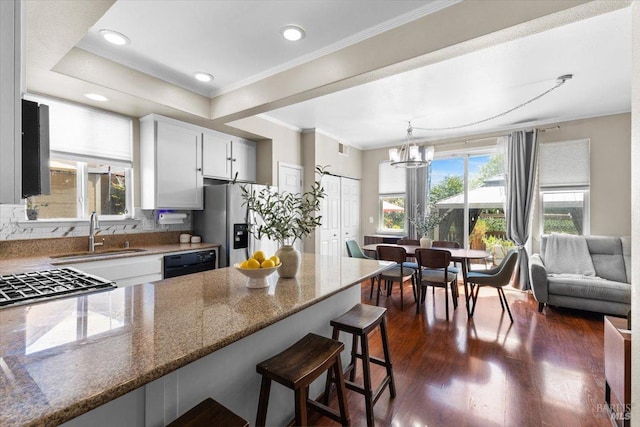 kitchen with dark wood-style flooring, stone countertops, a sink, dishwasher, and a notable chandelier