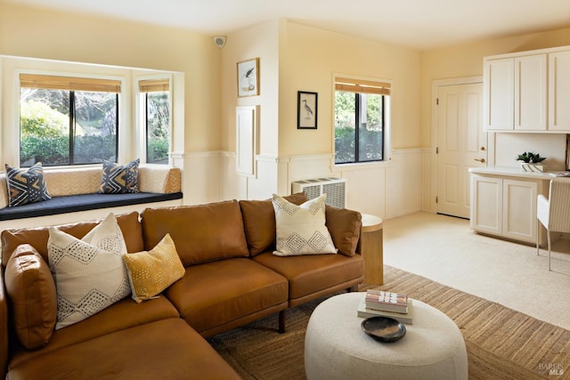 living room with an AC wall unit, light carpet, and a wainscoted wall