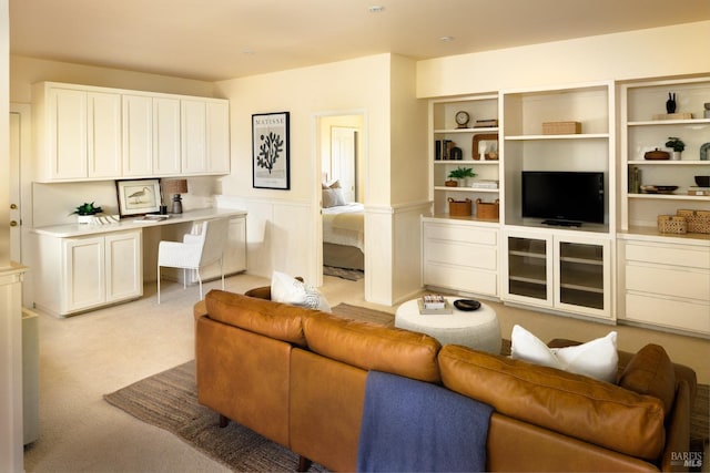 living room featuring light colored carpet, wainscoting, and built in study area