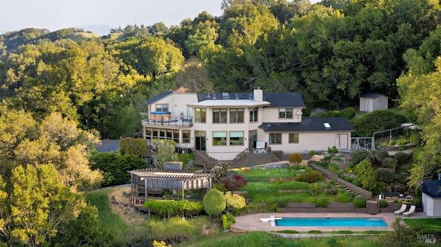 rear view of property featuring an outbuilding, a balcony, a shed, a pergola, and stairs