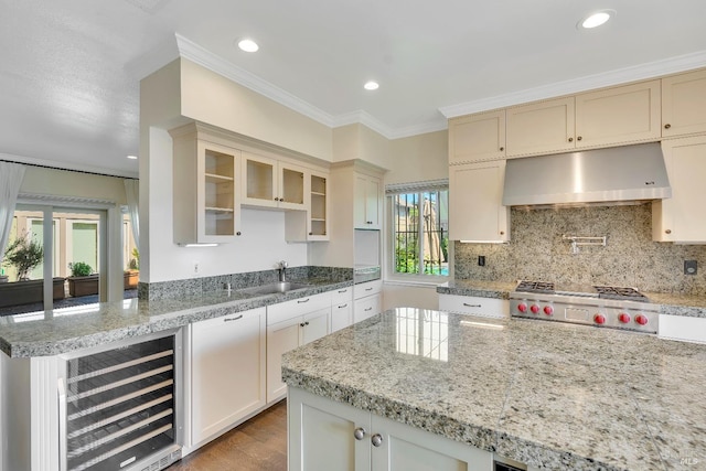 kitchen featuring glass insert cabinets, beverage cooler, under cabinet range hood, a sink, and light wood finished floors