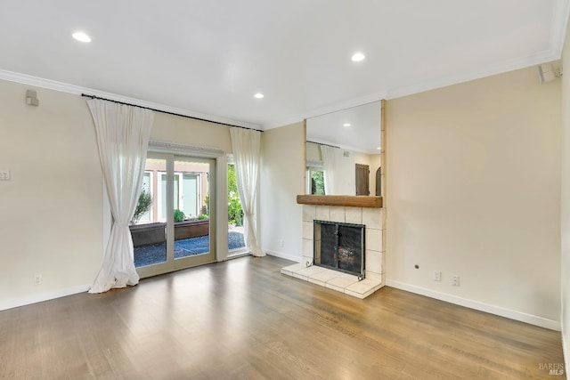 unfurnished living room with baseboards, ornamental molding, wood finished floors, and a tile fireplace