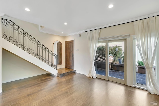 unfurnished living room with crown molding, arched walkways, wood finished floors, baseboards, and stairs