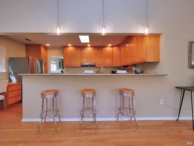 kitchen with under cabinet range hood, light wood-style flooring, a breakfast bar, and recessed lighting