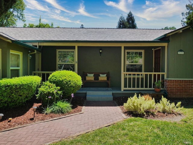 doorway to property featuring covered porch, roof with shingles, and board and batten siding