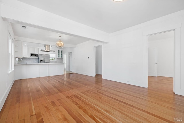 unfurnished living room with light wood-type flooring, a sink, baseboards, and a notable chandelier