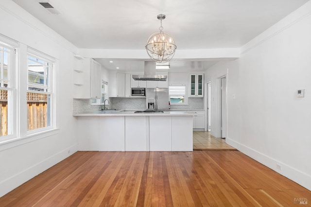 kitchen featuring appliances with stainless steel finishes, a sink, light countertops, a peninsula, and backsplash