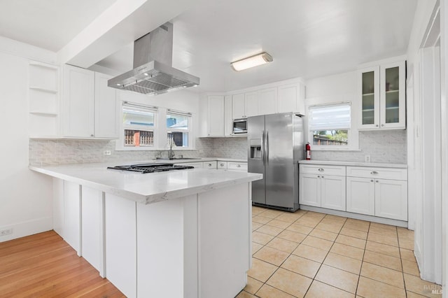kitchen featuring a peninsula, island range hood, stainless steel fridge, gas stovetop, and white cabinets