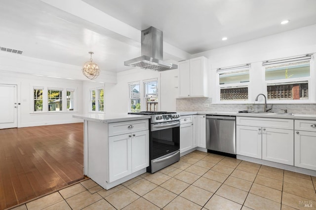 kitchen featuring island range hood, appliances with stainless steel finishes, a sink, light countertops, and a peninsula