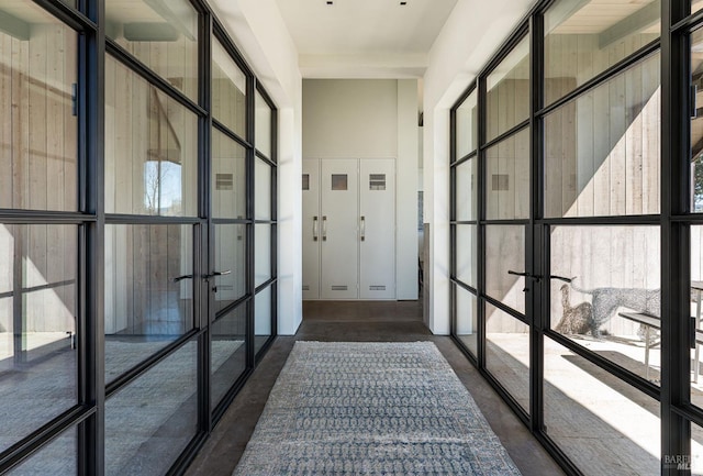hallway with concrete flooring, french doors, and a towering ceiling