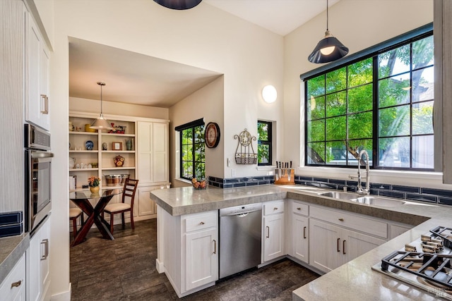 kitchen featuring a peninsula, white cabinets, a sink, appliances with stainless steel finishes, and hanging light fixtures