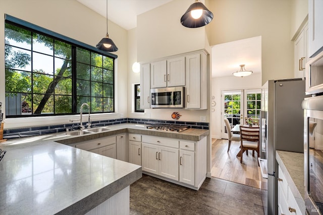 kitchen featuring white cabinets, a high ceiling, appliances with stainless steel finishes, a sink, and pendant lighting