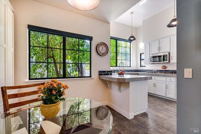 kitchen with a peninsula, a kitchen bar, white cabinetry, appliances with stainless steel finishes, and decorative light fixtures