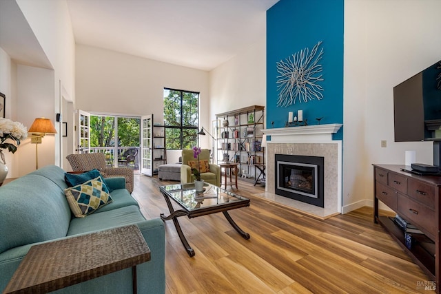 living area with wood finished floors, baseboards, a tile fireplace, and a towering ceiling