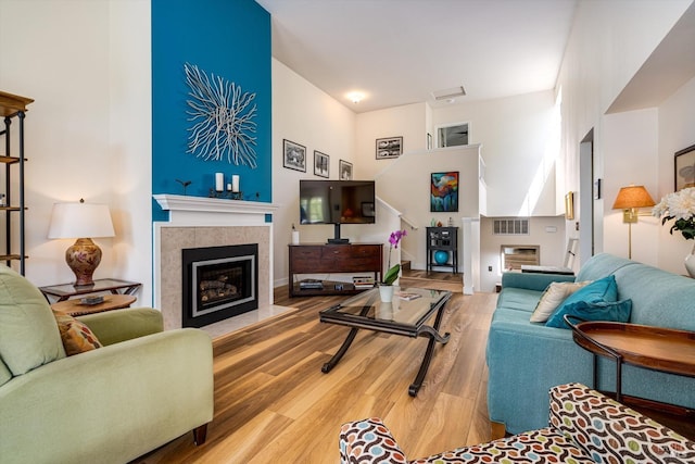 living room featuring a towering ceiling, visible vents, wood finished floors, and a tile fireplace