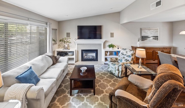 living room with a glass covered fireplace, visible vents, and vaulted ceiling