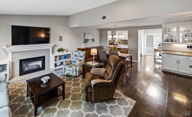 living area featuring visible vents, lofted ceiling, dark wood-type flooring, and a glass covered fireplace