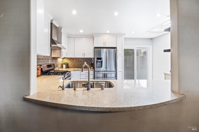 kitchen with a sink, a peninsula, wall chimney range hood, and appliances with stainless steel finishes