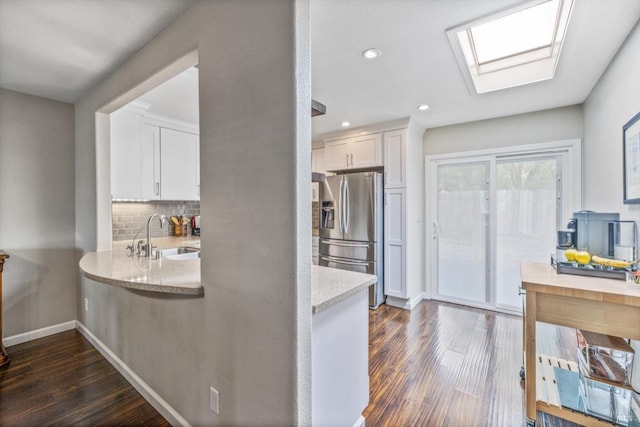 kitchen with light stone counters, dark wood finished floors, a sink, white cabinetry, and stainless steel fridge with ice dispenser