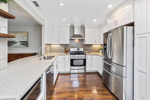 kitchen featuring dark wood-style flooring, a sink, wall chimney exhaust hood, stainless steel appliances, and white cabinets