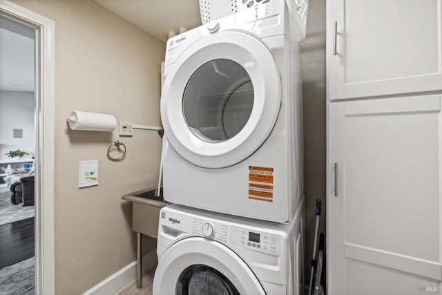 laundry room with laundry area, stacked washer and clothes dryer, baseboards, and wood finished floors