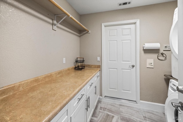 washroom with stacked washer / dryer, laundry area, baseboards, and visible vents