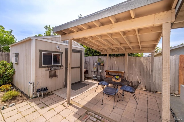 view of patio with an outdoor structure, outdoor dining area, fence, and a storage unit