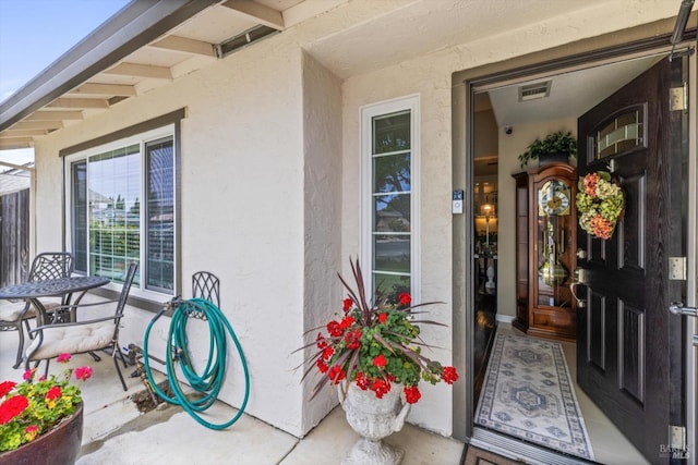 property entrance featuring stucco siding and visible vents