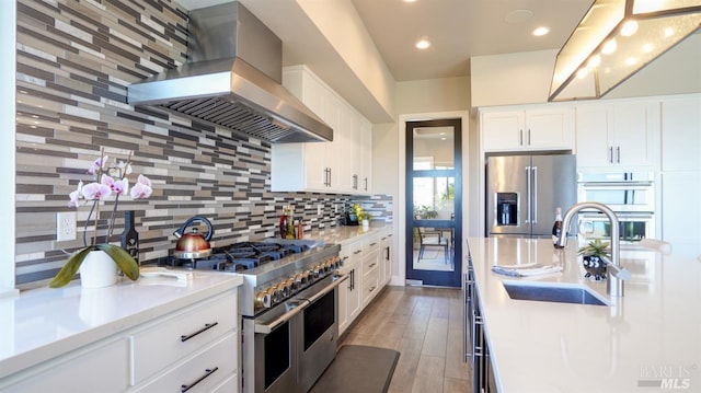 kitchen featuring wall chimney range hood, appliances with stainless steel finishes, a sink, light countertops, and backsplash