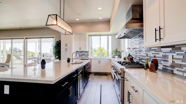 kitchen with light countertops, double oven range, wall chimney exhaust hood, and plenty of natural light