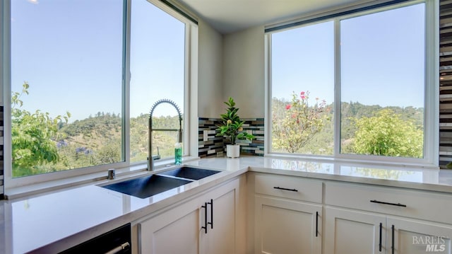 kitchen featuring a sink, white cabinetry, backsplash, and light countertops