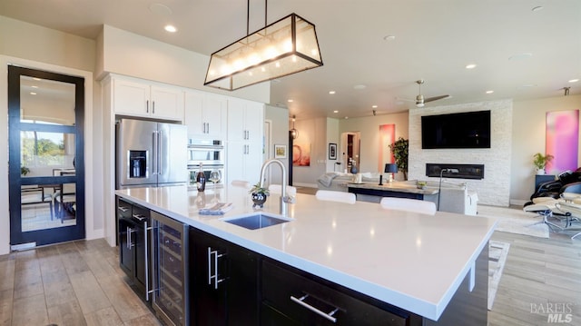 kitchen with beverage cooler, open floor plan, ceiling fan, light wood-type flooring, and a sink