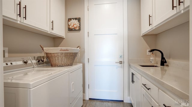 washroom featuring cabinet space, a sink, washer and clothes dryer, and light wood finished floors