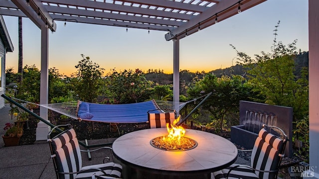 patio terrace at dusk featuring a pergola and an outdoor fire pit