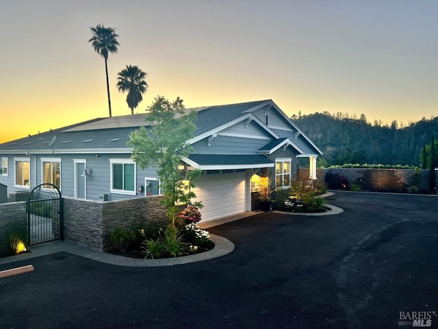 craftsman-style home featuring aphalt driveway, fence, stone siding, and roof with shingles