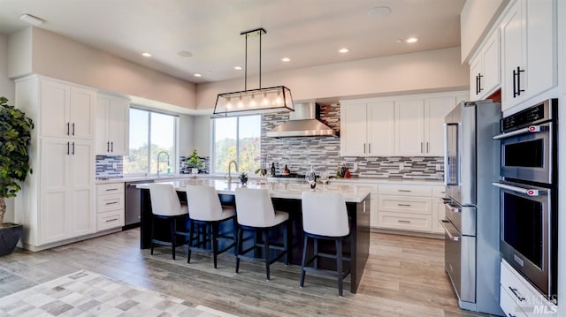 kitchen with wall chimney range hood, stainless steel appliances, a breakfast bar, and light countertops