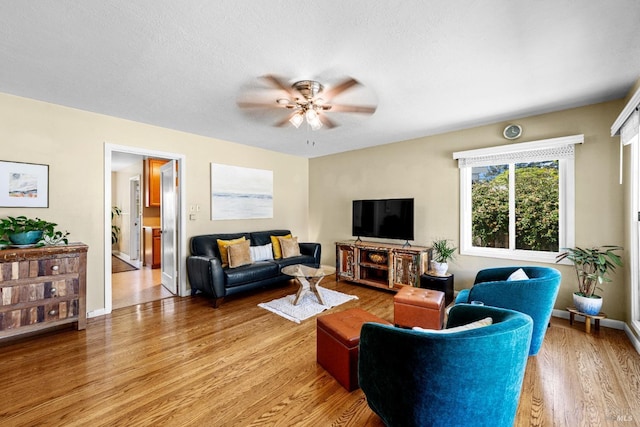 living room featuring baseboards, a ceiling fan, and light wood finished floors