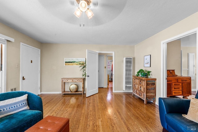 living area with ceiling fan, light wood-style floors, a heating unit, baseboards, and visible vents