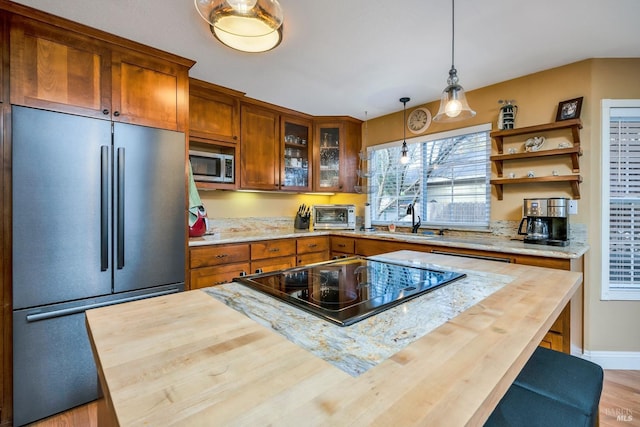 kitchen with brown cabinets, hanging light fixtures, appliances with stainless steel finishes, butcher block counters, and glass insert cabinets