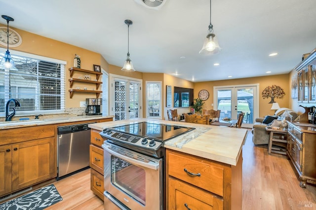 kitchen with pendant lighting, open floor plan, a sink, light wood-style flooring, and stainless steel appliances