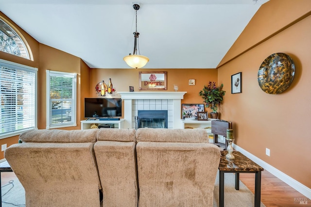living room featuring baseboards, light wood-style floors, vaulted ceiling, and a fireplace