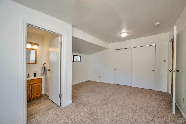 unfurnished bedroom with baseboards, ensuite bathroom, a closet, and light colored carpet