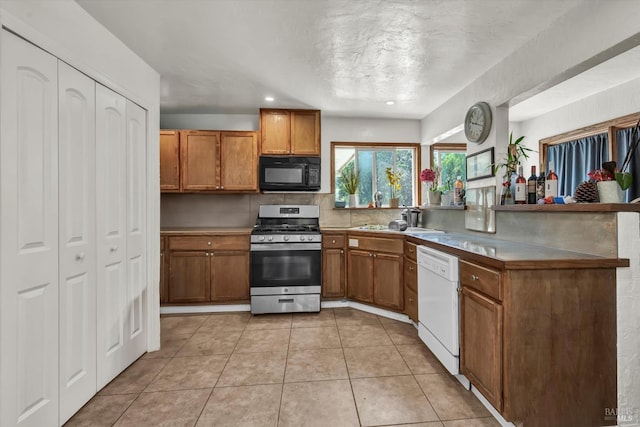 kitchen with black microwave, dishwasher, stainless steel range with gas stovetop, brown cabinetry, and a peninsula