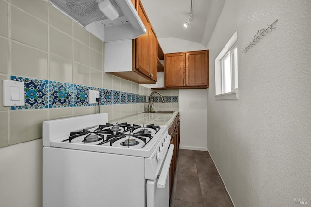 kitchen featuring brown cabinetry, white range with gas cooktop, tasteful backsplash, a sink, and exhaust hood