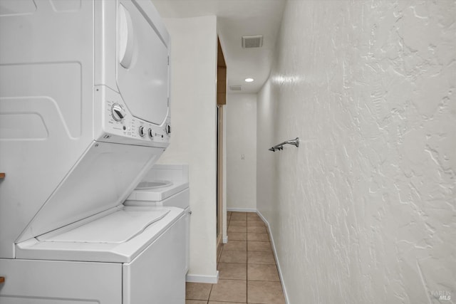 clothes washing area with stacked washer / drying machine, laundry area, baseboards, light tile patterned floors, and visible vents