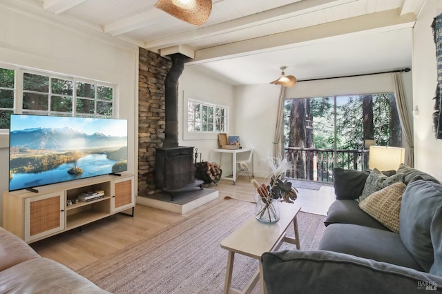 living area featuring beamed ceiling, a wood stove, and wood finished floors